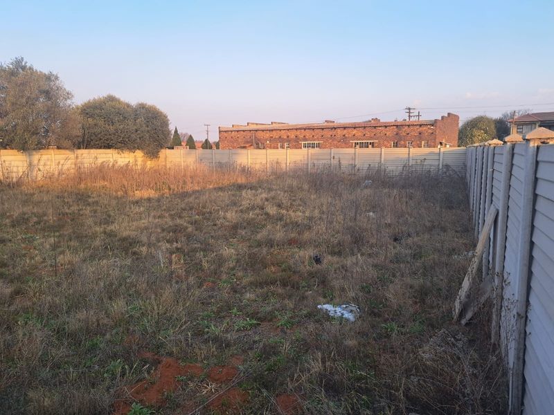 A vacant commercial plot featuring a precast concrete boundary wall and overgrown vegetation, offering a blank canvas for future development.
