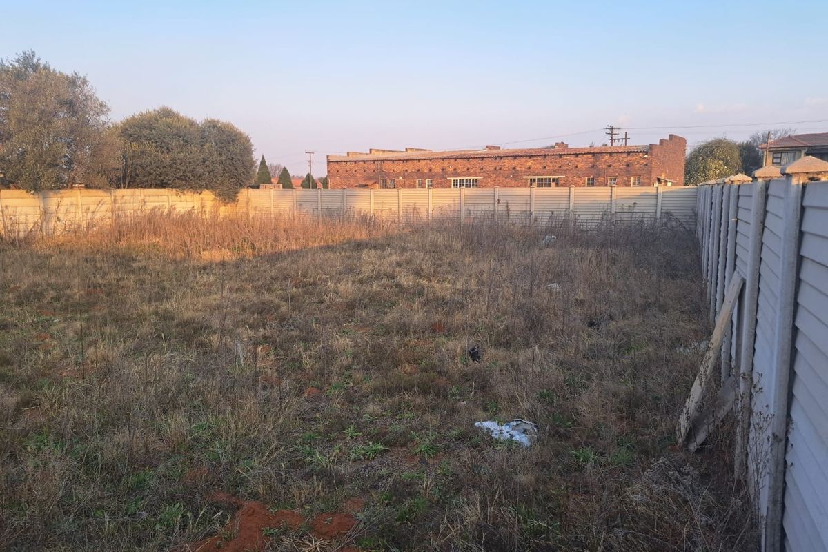 A vacant commercial plot featuring a precast concrete boundary wall and overgrown vegetation, offering a blank canvas for future development.