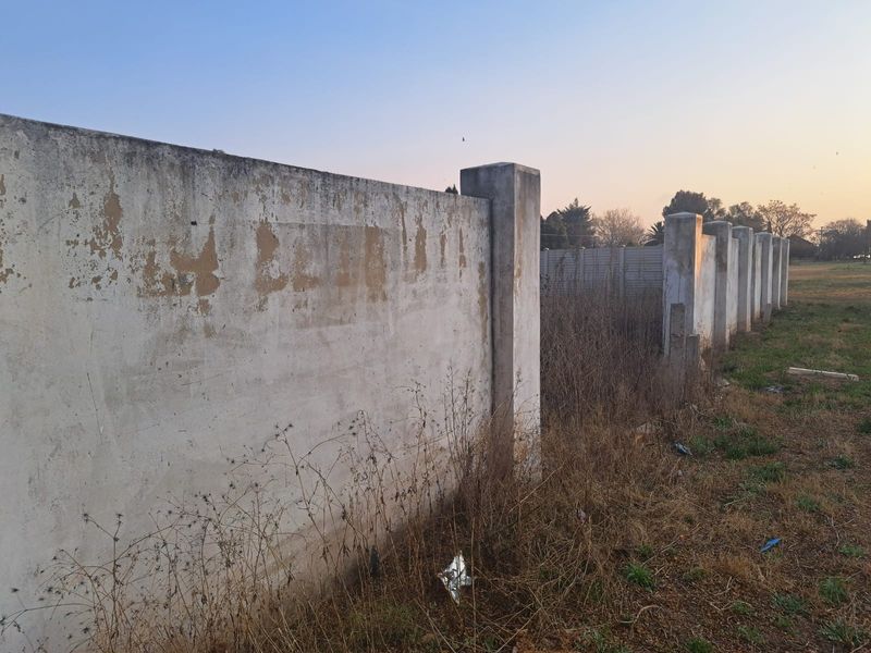 A view of the perimeter boundary wall on the vacant commercial land, showing signs of weathering and peeling paint on the concrete structure.