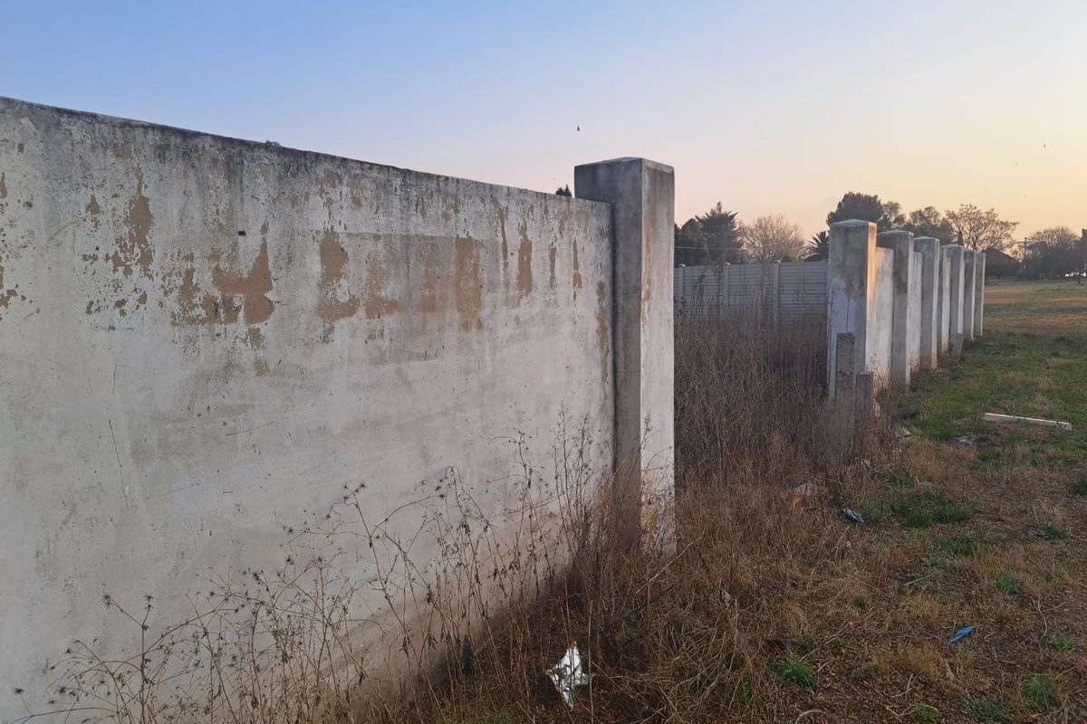 A view of the perimeter boundary wall on the vacant commercial land, showing signs of weathering and peeling paint on the concrete structure.