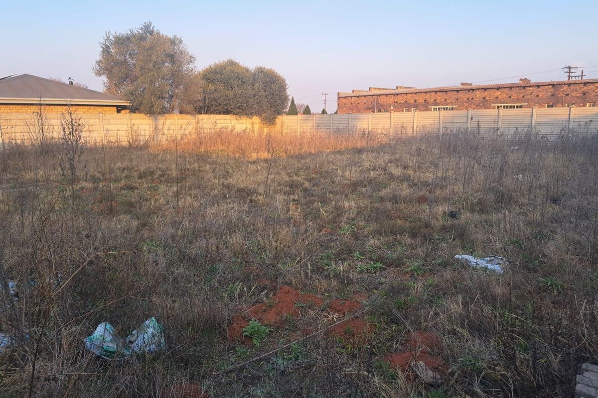 A view of a vacant commercial plot featuring dry, overgrown vegetation and enclosed by a precast concrete boundary wall.