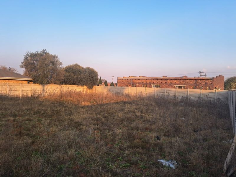 A vacant commercial land plot featuring overgrown grass and enclosed by a precast concrete boundary wall.