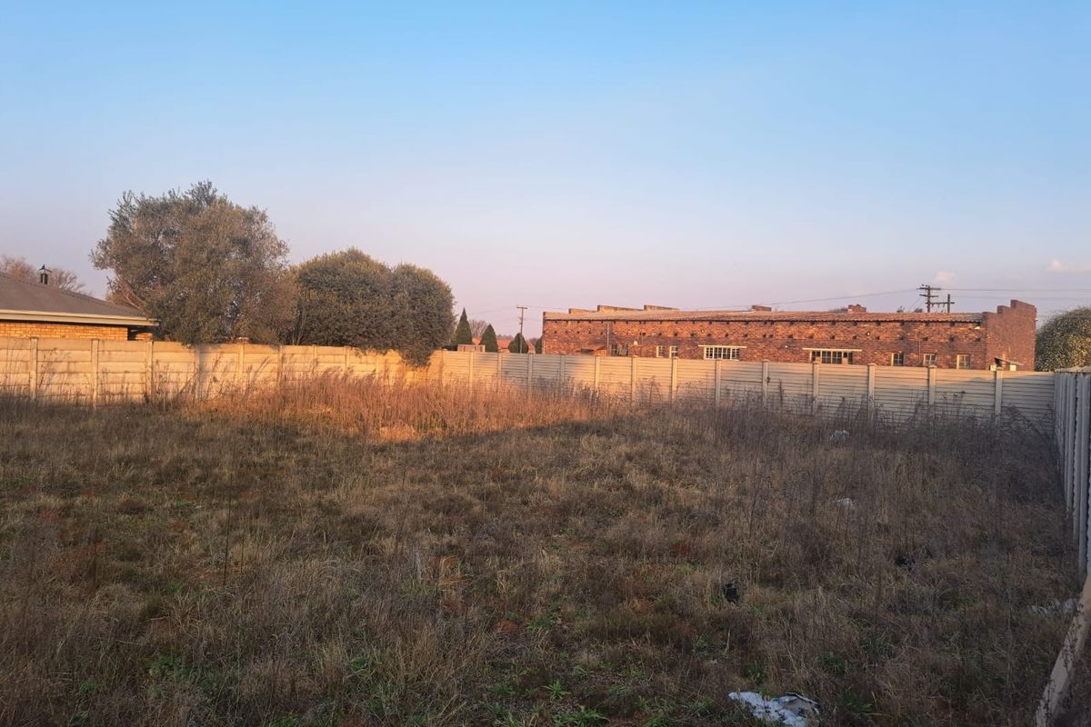 A vacant commercial land plot featuring overgrown grass and enclosed by a precast concrete boundary wall.