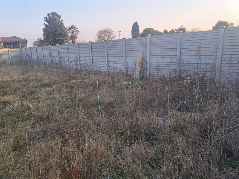 A view of a vacant commercial plot featuring a precast concrete boundary wall and overgrown vegetation.