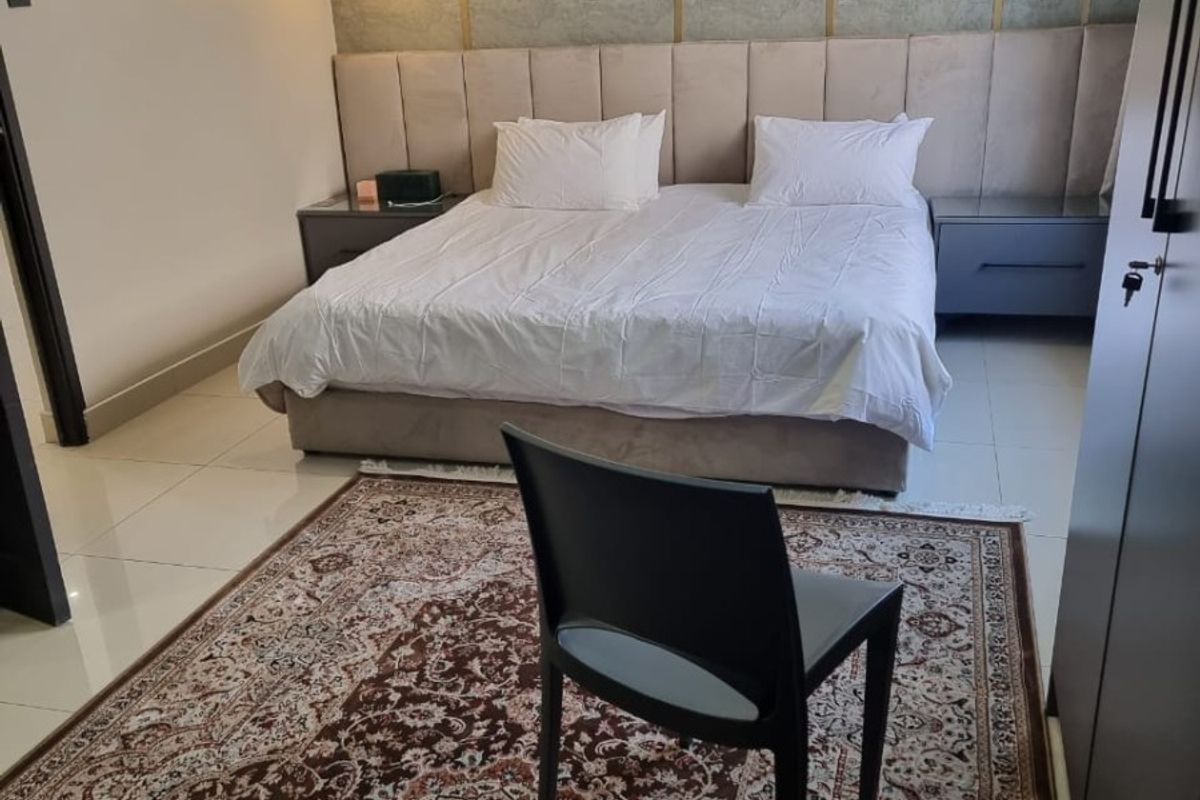 A well-maintained bedroom featuring a large upholstered headboard, tiled flooring, and built-in wardrobe storage.
