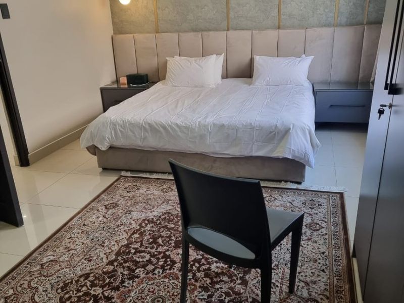 A well-maintained bedroom featuring a large upholstered headboard, tiled flooring, and built-in wardrobe storage.