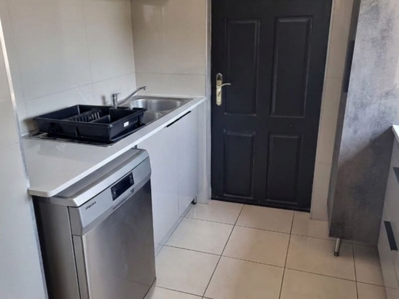A compact, modern scullery featuring sleek cabinetry, tiled flooring, a stainless steel sink, and an integrated dishwasher.
