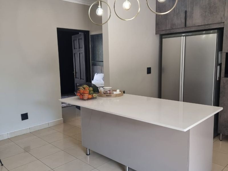 Modern kitchen featuring a central island with a quartz countertop, sleek cabinetry, and contemporary pendant lighting, complemented by neutral tiled flooring.