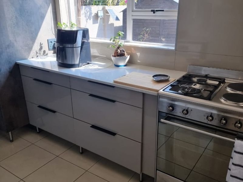 Modern kitchen featuring sleek grey cabinetry, stone countertops, a gas cooktop, and an integrated oven, illuminated by natural light from a large window.