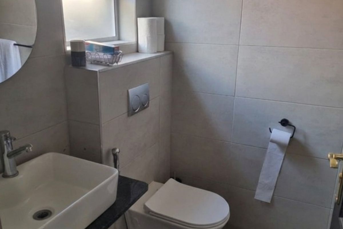 A modern bathroom featuring a wall-mounted toilet with a concealed cistern, a vessel sink on a granite vanity, and neutral wall tiling.
