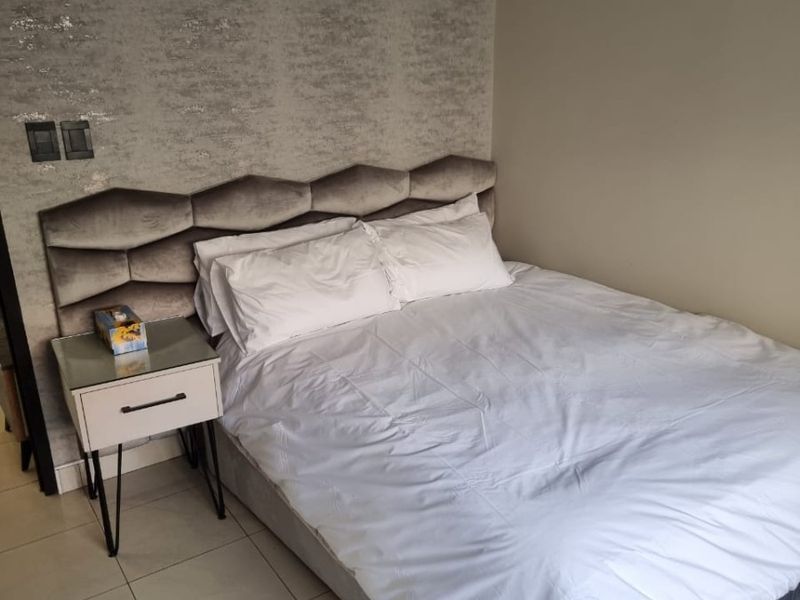 A bedroom featuring tiled flooring and a textured feature wall behind the bed area.