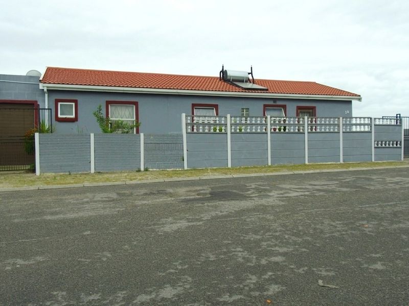 A single-story residential property featuring a tiled roof, solar water heater, and a secure precast concrete boundary wall with gated access.