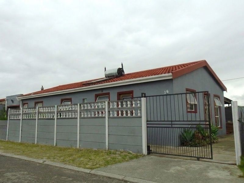 Front exterior view of a single-story house featuring a tiled roof, solar geyser, and secure perimeter wall with a metal gate.