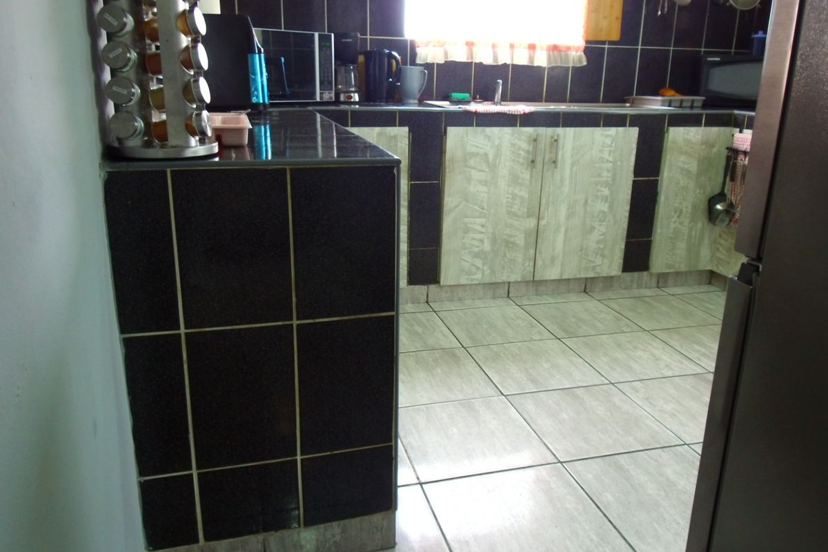 A functional kitchen featuring dark tiled countertops, light-toned cabinetry, and neutral floor tiles, providing a practical workspace for daily meal preparation.