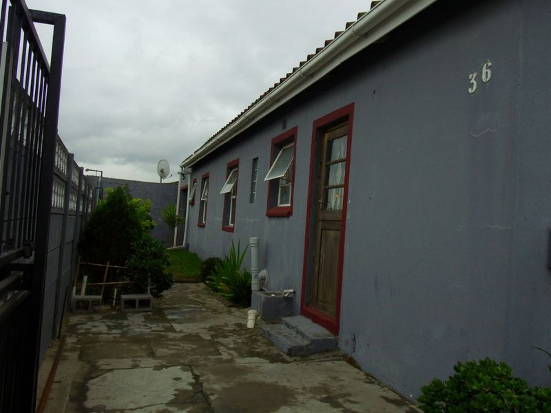 A side view of the property showing a paved walkway, boundary wall, and exterior access door with security gate.