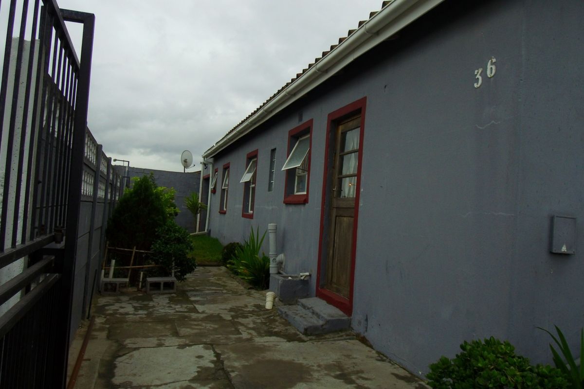 A side view of the property showing a paved walkway, boundary wall, and exterior access door with security gate.