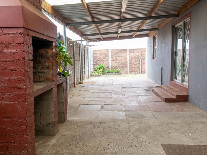 Covered outdoor patio area featuring a built-in brick braai, paved flooring, and direct access to the home via a sliding glass door.