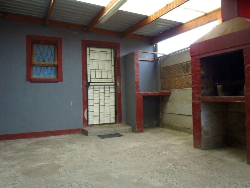 Covered outdoor patio area featuring a built-in brick braai, concrete flooring, and a security gate entrance.