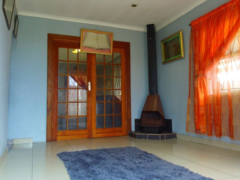 A living room featuring tiled flooring, a corner-mounted freestanding fireplace, and wooden French doors leading to an adjacent space.