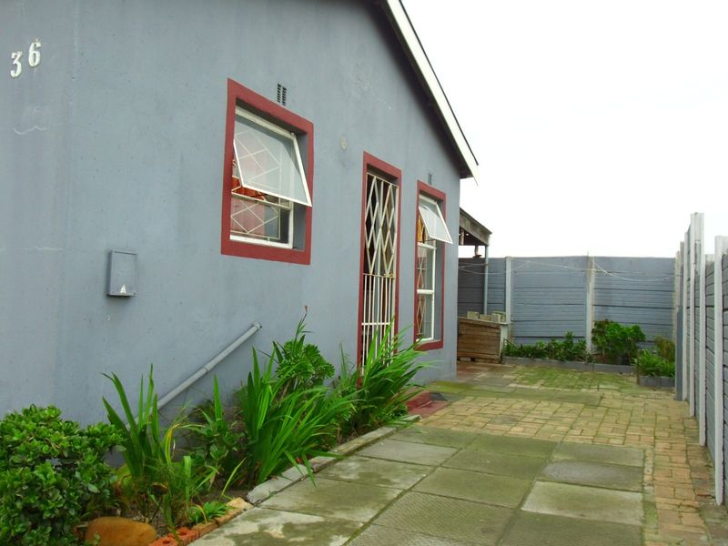 Rear exterior view of the property featuring a paved patio area, precast concrete boundary walls, and secure window and door access.