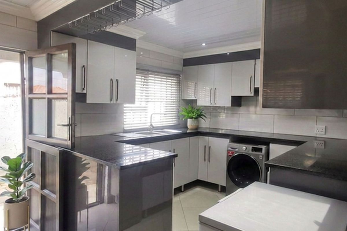 Modern kitchen featuring sleek two-tone cabinetry, granite countertops, tiled backsplash, and direct access to an outdoor patio area.