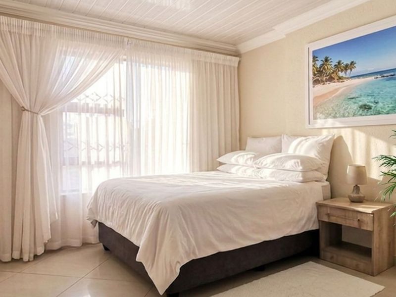 A well-lit bedroom featuring tiled flooring, a textured tongue and groove ceiling, and a large sliding door providing natural light.