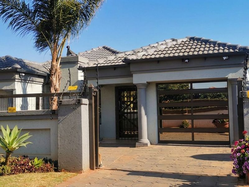 Front elevation of a modern house featuring a paved driveway, secure garage access, and perimeter boundary wall with electric fencing.