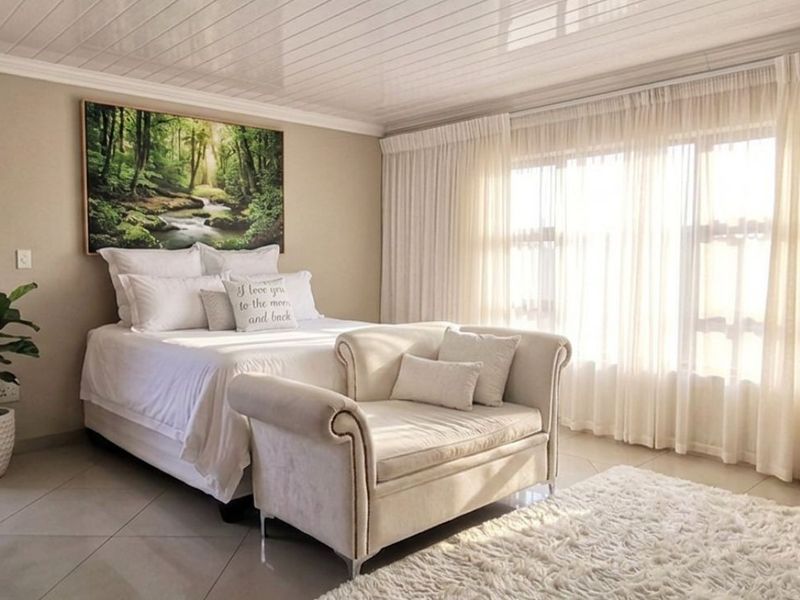 A bright and spacious bedroom featuring neutral tiled flooring, a clean tongue and groove ceiling, and large windows with floor-to-ceiling curtains.