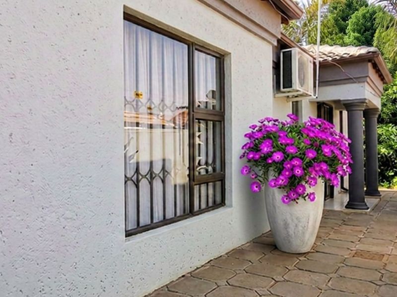 A well-maintained rear exterior area featuring a paved patio, secure window bars, and an external air conditioning unit.
