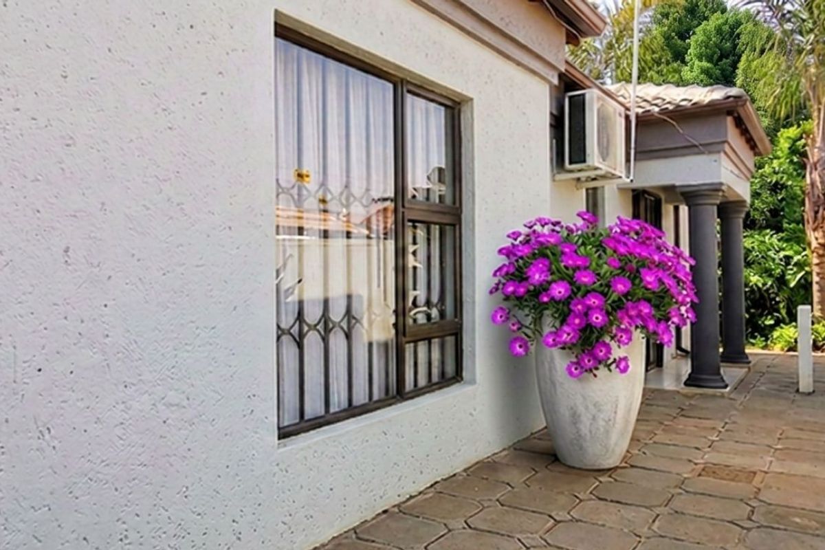 A well-maintained rear exterior area featuring a paved patio, secure window bars, and an external air conditioning unit.