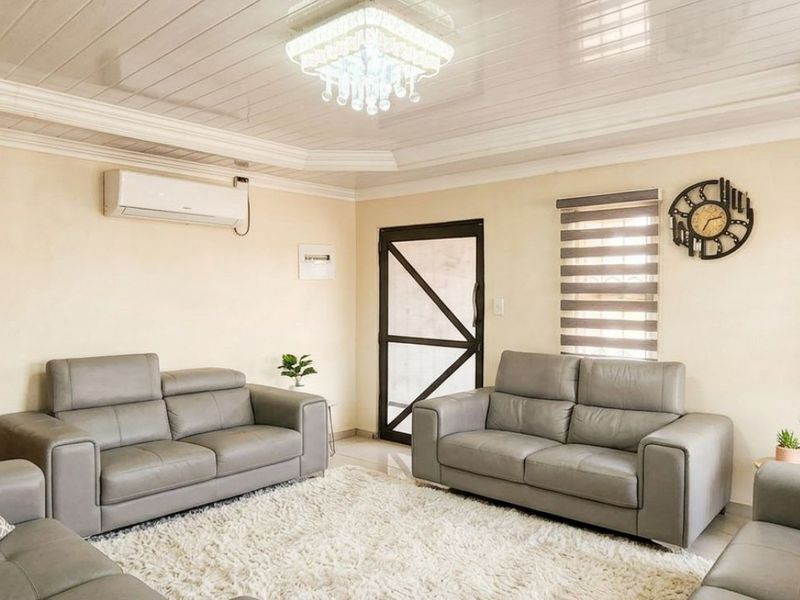 A well-maintained living room featuring a coffered ceiling, crystal chandelier, split-system air conditioning, and neutral wall finishes.