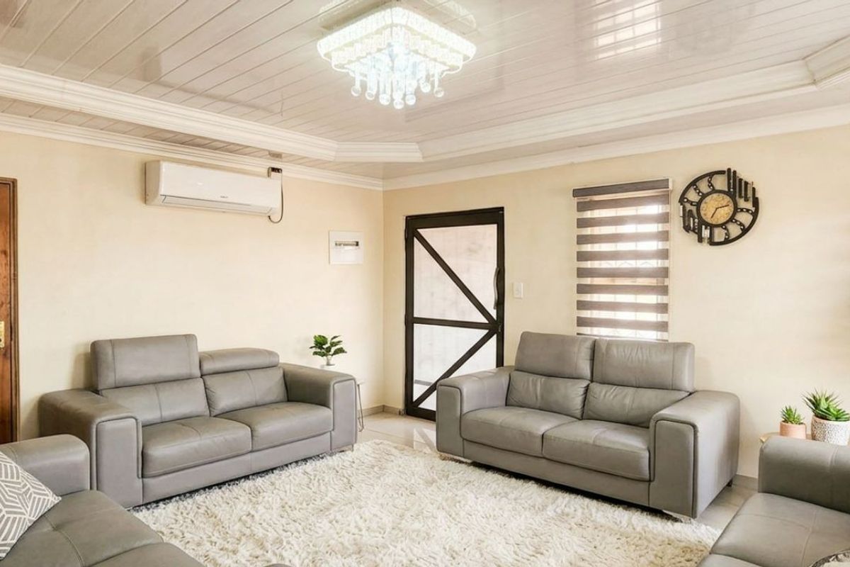 A well-maintained living room featuring a coffered ceiling, crystal chandelier, split-system air conditioning, and neutral wall finishes.