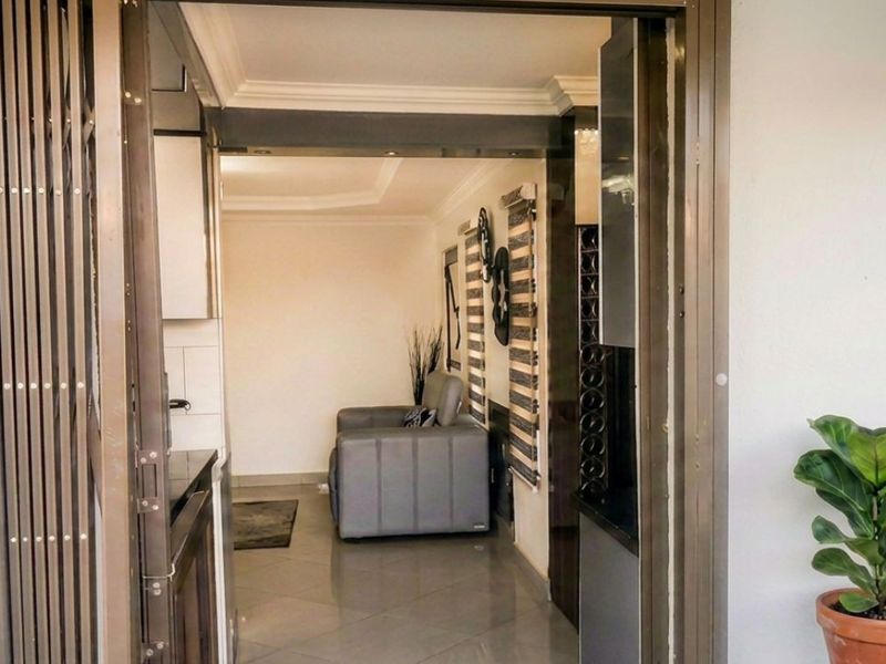 View through a sliding security gate into a tiled interior space featuring recessed lighting and crown molding.