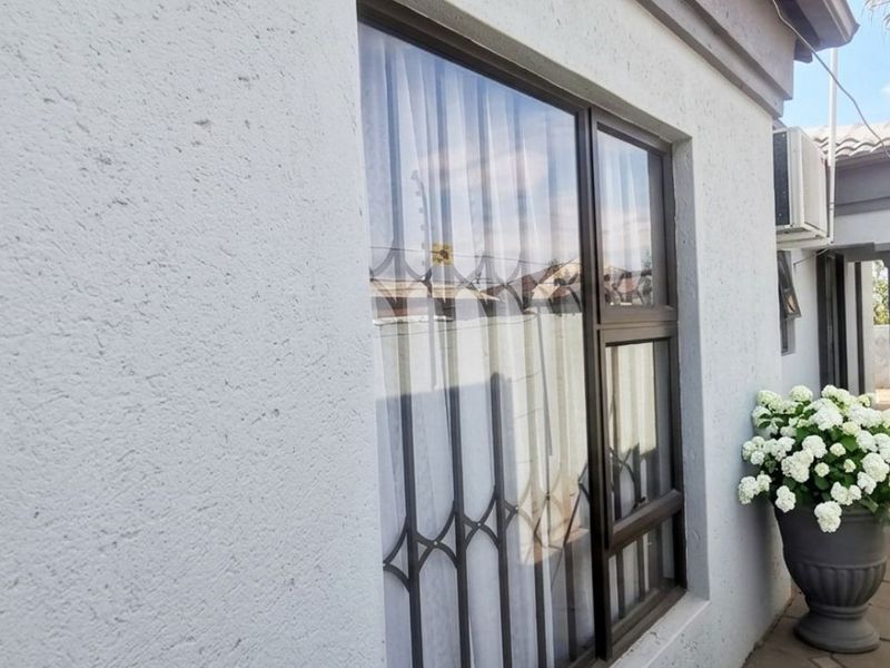 A view of the side exterior of the house featuring textured plaster walls, aluminium window frames with security gates, and a paved walkway.