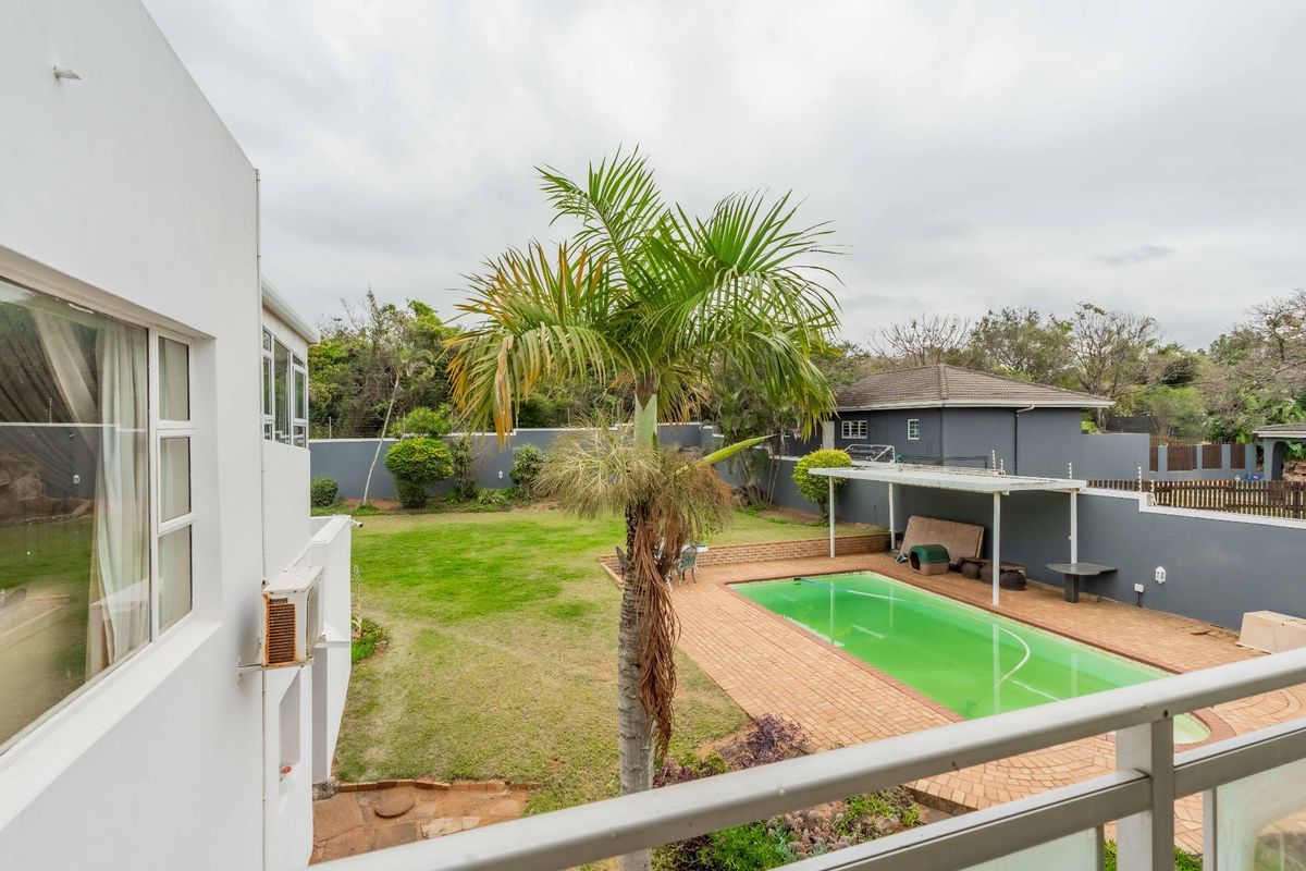 Rear garden view featuring a swimming pool with a brick paved deck, a covered patio area, and a surrounding boundary wall.