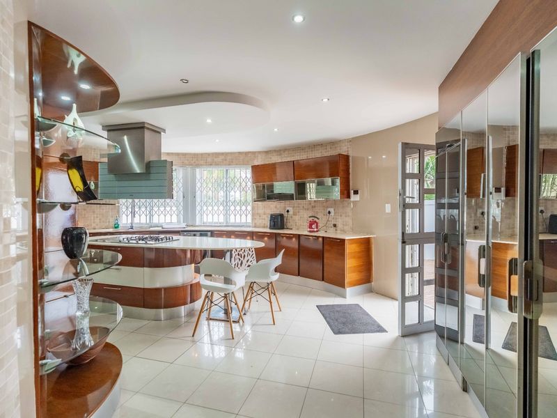 Spacious kitchen featuring a unique curved island, built-in cabinetry, gas hob with extractor, and tiled flooring with modern recessed lighting.