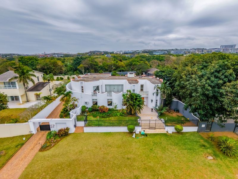 Aerial view of a large white multi-level residential property featuring a landscaped front garden, paved driveway, and secure perimeter fencing.