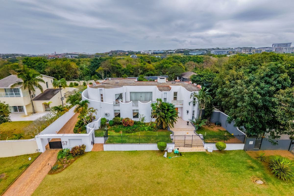 Aerial view of a large white multi-level residential property featuring a landscaped front garden, paved driveway, and secure perimeter fencing.