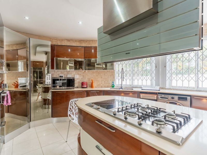 Modern kitchen featuring a central island with gas cooktop, integrated appliances, sleek cabinetry, and tiled backsplash with security-fitted windows.