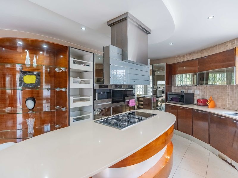Modern kitchen featuring a curved island with integrated gas cooktop, stainless steel extractor fan, built-in ovens, and ample wood-finish cabinetry.