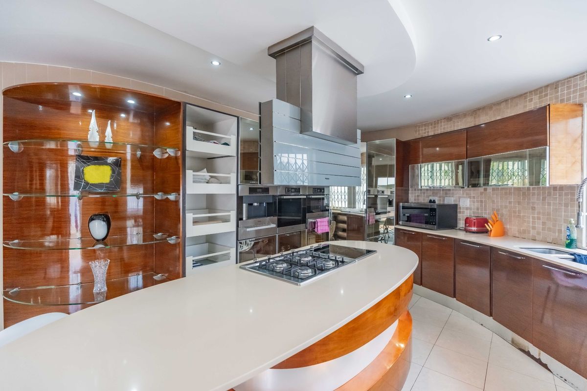Modern kitchen featuring a curved island with integrated gas cooktop, stainless steel extractor fan, built-in ovens, and ample wood-finish cabinetry.