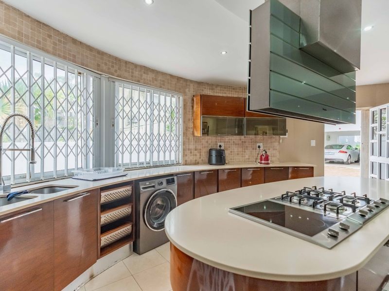 Modern kitchen featuring dark wood cabinetry, stone countertops, a central island with a gas hob, and integrated appliances with security gates on windows.