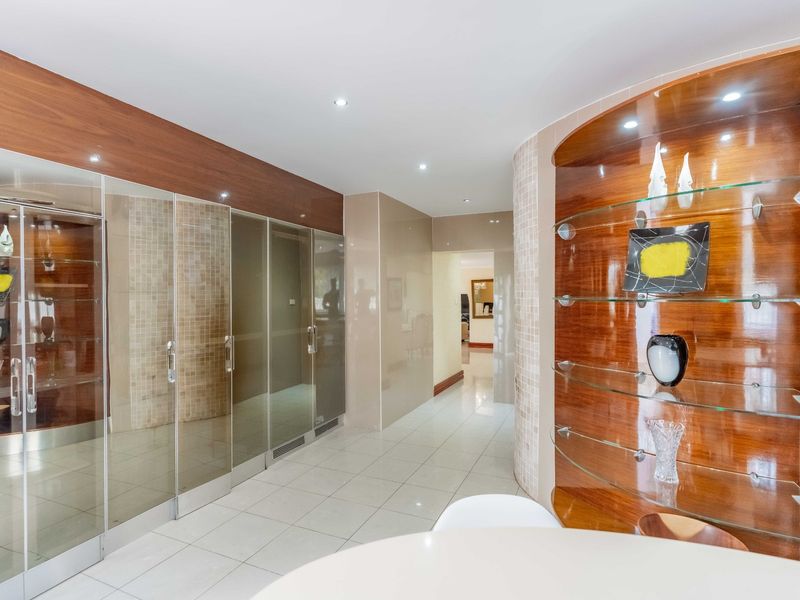 A modern hallway featuring tiled flooring, recessed downlights, and extensive built-in mirrored cabinetry with integrated glass display shelving.