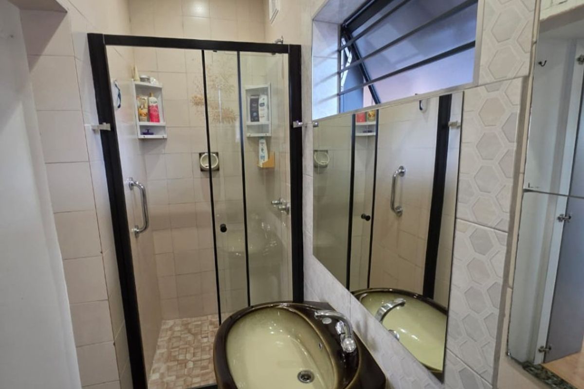 A functional bathroom featuring a pedestal basin, a glass-enclosed shower, and tiled finishes throughout with a louvered window for ventilation.