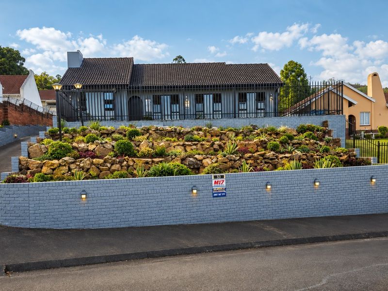 Front elevation of a house featuring a tiered landscaped rockery, paved driveway, and secure perimeter fencing with integrated wall lighting.