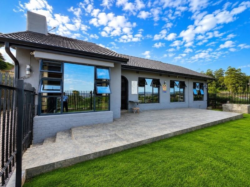 Rear view of the house featuring a spacious tiled patio, well-maintained lawn, and modern aluminium-framed windows under a tiled roof.