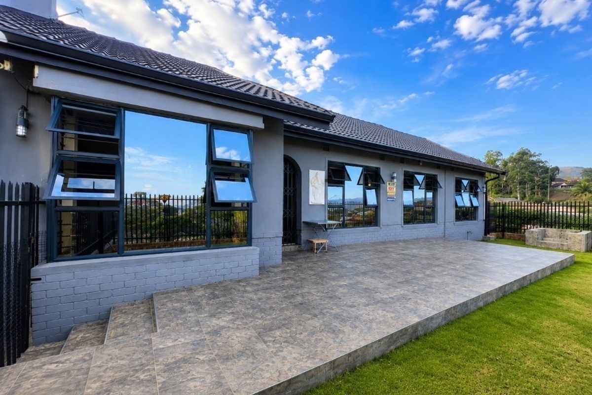 A well-maintained rear exterior view featuring a spacious tiled patio, modern aluminium windows, and a neat garden area.