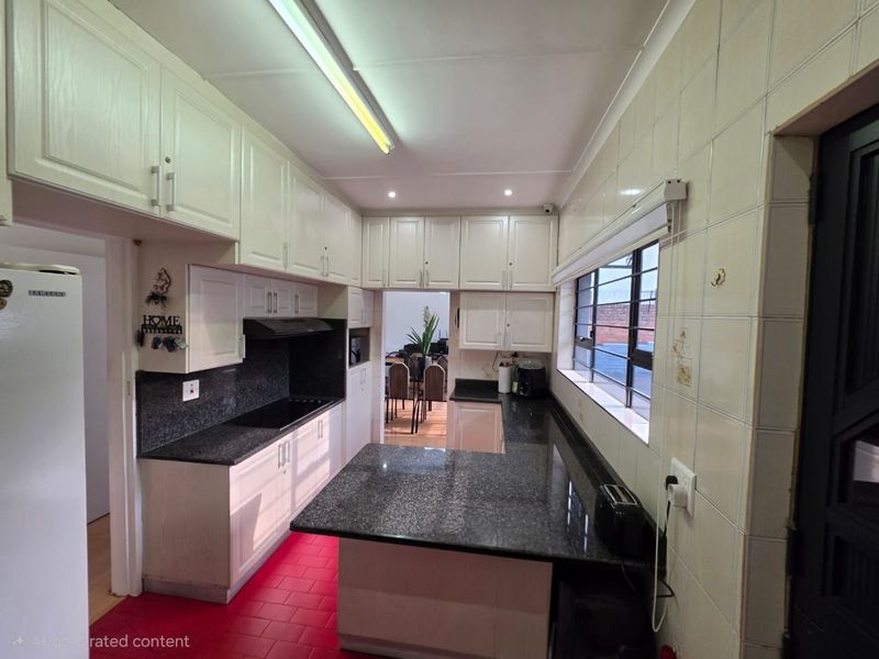 Functional kitchen featuring granite countertops, ample built-in cabinetry, an electric hob with extractor fan, and tiled wall finishes.