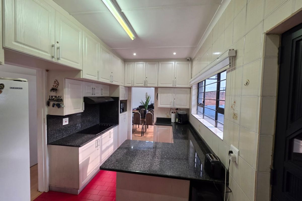 Functional kitchen featuring granite countertops, ample built-in cabinetry, an electric hob with extractor fan, and tiled wall finishes.