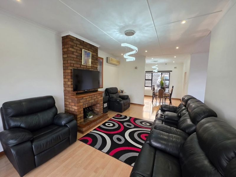 Open-plan living and dining area featuring a prominent brick fireplace, laminate flooring, and modern lighting fixtures.